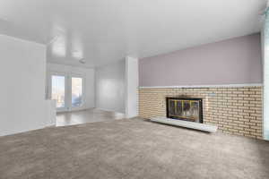 Unfurnished living room featuring light colored carpet and a brick fireplace