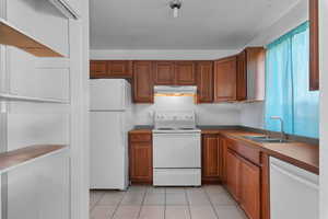 Kitchen with white appliances, wood finish cabinets, light tile patterned floors, and dark countertops