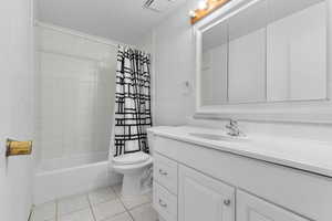 Bathroom featuring a textured wall, vanity, light tile patterned floors, shower / bath combination with curtain, and a textured ceiling