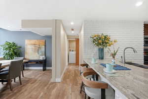 Kitchen with light stone counters, light wood finished floors, a kitchen breakfast bar, brick wall, and recessed lighting