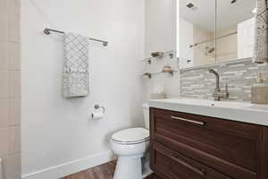 Full bath with vanity, a tile shower, wood finished floors, and decorative backsplash