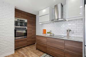 Kitchen with light stone countertops, modern cabinets, double oven, light wood-type flooring, and black electric stovetop