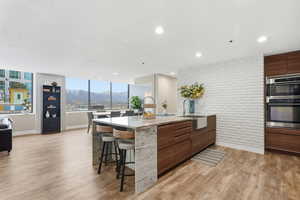Kitchen with modern cabinets, brick wall, a mountain view, light stone counters, and a center island with sink