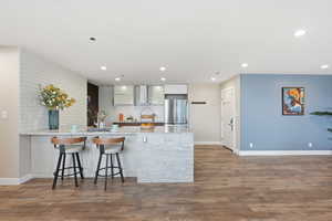 Kitchen with a peninsula, light stone counters, light wood-type flooring, freestanding refrigerator, and a breakfast bar area