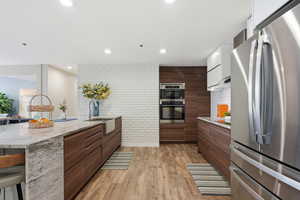 Kitchen with light stone countertops, stainless steel appliances, light wood finished floors, a breakfast bar area, and modern cabinets