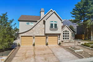 View of front of house featuring stucco siding, stone siding, a chimney, and driveway