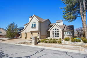 View of front of house featuring stone siding, a chimney, stucco siding, concrete driveway, and a garage