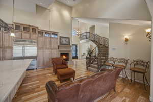 Living room featuring light wood-type flooring, a lit fireplace, suspended lighting, and a high ceiling