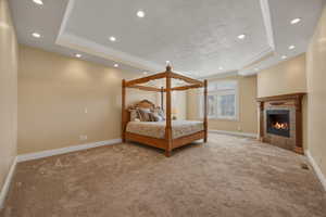 Bedroom featuring a raised ceiling, crown molding, light colored carpet, a fireplace, and recessed lighting