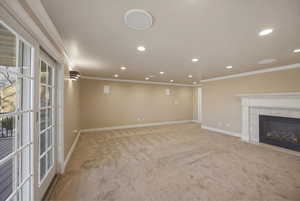 Unfurnished living room featuring a tiled fireplace, crown molding, light carpet, and recessed lighting