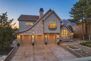 French provincial home with stone siding, stucco siding, a chimney, and driveway