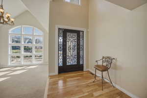 Foyer with light wood-style flooring, hanging lights, and a high ceiling