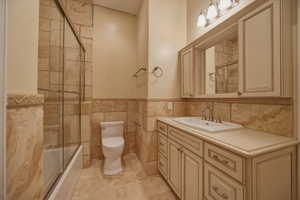 Bathroom featuring vanity, bath / shower combo with glass door, tile walls, and wainscoting