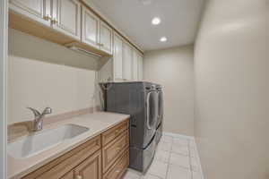 Laundry area with independent washer and dryer, recessed lighting, cabinet space, and light tile patterned floors