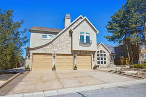View of front facade with stone siding, stucco siding, driveway, and a chimney