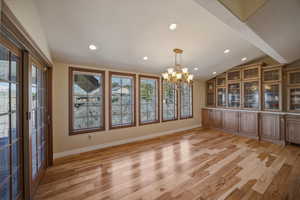 Unfurnished dining area featuring light wood-style floors, suspended lighting, and vaulted ceiling