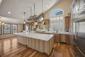 Kitchen featuring stainless steel appliances, tasteful backsplash, a spacious island, light wood-style flooring, and vaulted ceiling