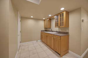 Kitchen featuring glass insert cabinets, recessed lighting, wood finish cabinetry, dark stone countertops, and light tile patterned floors