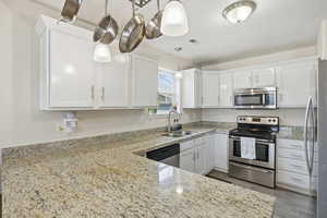 Kitchen featuring stainless steel appliances, light stone countertops, white cabinets, pendant lighting, and wood finished floors