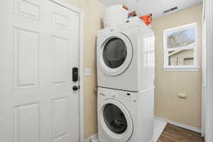 Laundry room with stacked washer / drying machine and wood finished floors