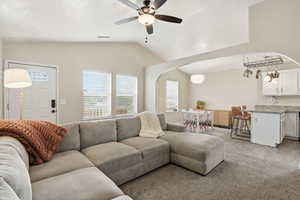 Living room with a ceiling fan, vaulted ceiling, healthy amount of natural light, light carpet, and arched walkways