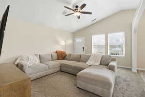 Living room featuring a ceiling fan, vaulted ceiling, carpet floors, and arched walkways