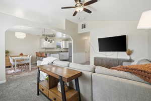 Carpeted living area with arched walkways, ceiling fan, vaulted ceiling, and a wainscoted wall