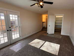Unfurnished bedroom featuring dark carpet, a spacious closet, access to exterior, french doors, and lofted ceiling
