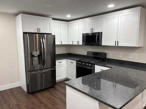 Kitchen featuring stainless steel appliances, dark stone countertops, white cabinetry, dark wood-type flooring, and a peninsula