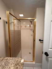 Bathroom with a textured ceiling, a shower stall, and light tile patterned floors