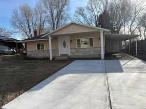 Bungalow with a porch, a carport, concrete driveway, and stone siding