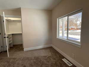 Unfurnished bedroom with a walk in closet, dark colored carpet, and a textured ceiling