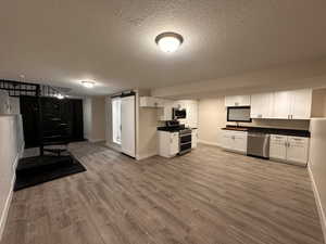 Kitchen featuring dark countertops, a textured ceiling, stainless steel appliances, white cabinetry, and light wood-style floors