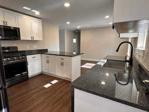 Kitchen with dark wood-style flooring, a peninsula, stainless steel appliances, dark stone countertops, and white cabinets
