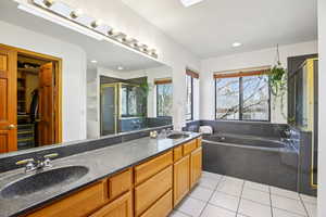 Full bathroom with double vanity, a walk in closet, a stall shower, light tile patterned floors, and a garden tub
