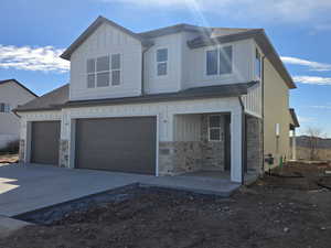 View of front of house with board and batten siding, stone siding, covered porch, and driveway