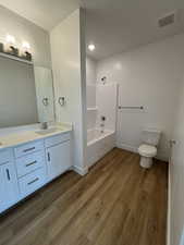 Full bathroom featuring double vanity, dark wood-style floors, and washtub / shower combination