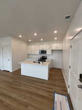 Kitchen featuring white cabinetry, dark wood-style flooring, stainless steel appliances, a center island with sink, and recessed lighting