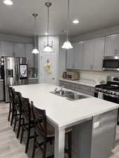 Kitchen with gray cabinets, a kitchen breakfast bar, light countertops, and a kitchen island with sink