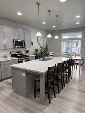 Kitchen with gray cabinetry, a breakfast bar area, stainless steel appliances, a center island with sink, and pendant lighting
