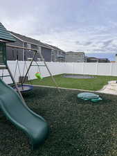 Fenced backyard featuring a playground and a trampoline