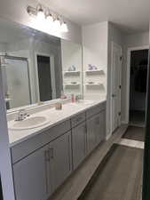 Bathroom featuring double vanity, a textured ceiling, light wood-style floors, a shower stall, and a walk in closet