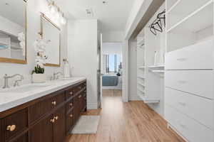 Ensuite bathroom featuring double vanity, light wood-style floors, and a closet