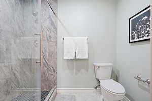 Full bathroom featuring toilet and a marble finish shower