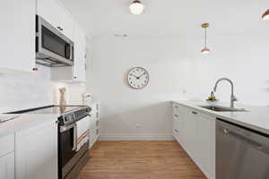 Kitchen featuring white cabinets, stainless steel appliances, light wood-style flooring, and light stone countertops