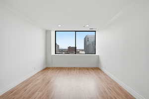 Empty room with ornamental molding, light wood-style flooring, a view of city, and recessed lighting