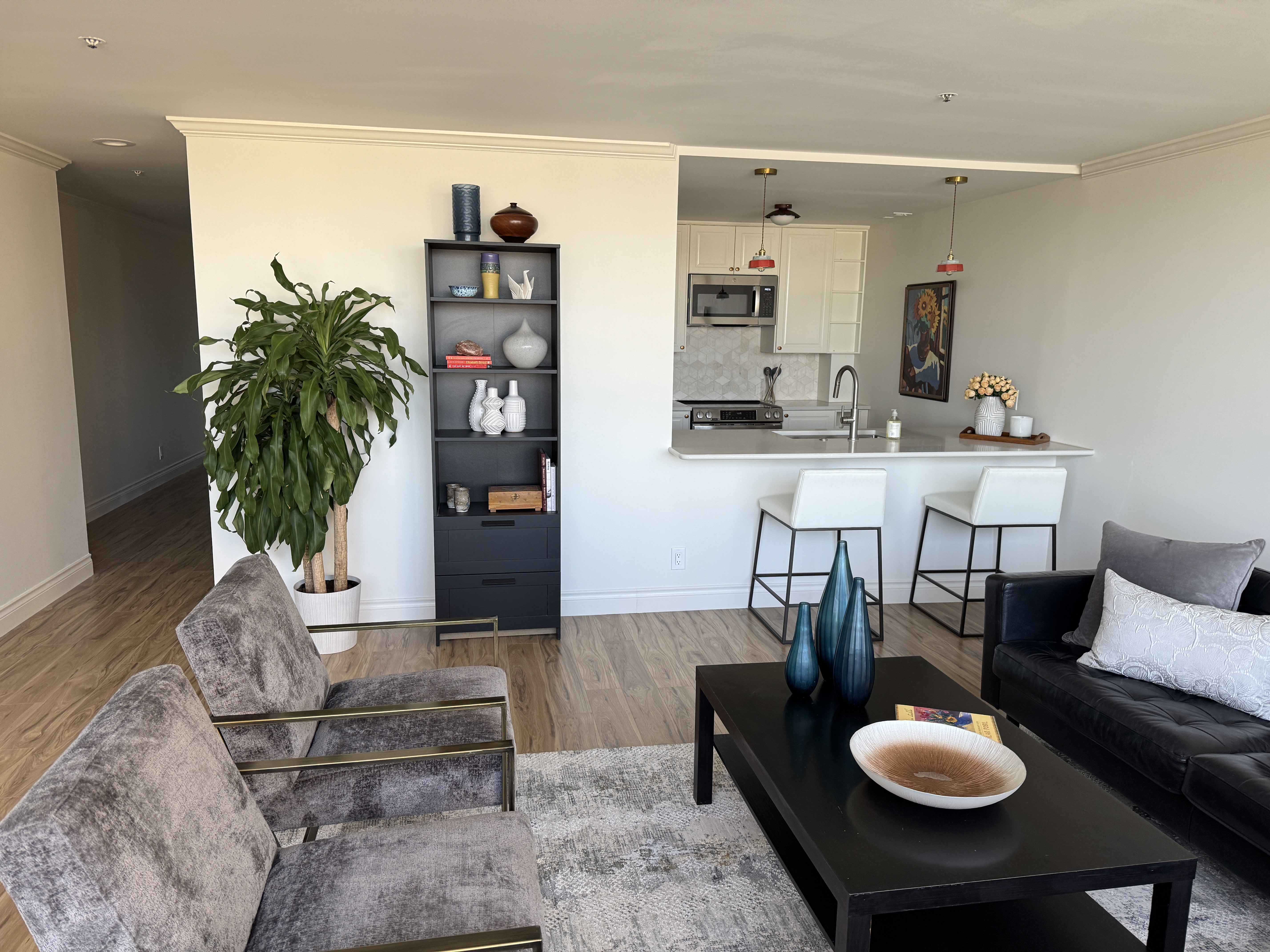 Open-concept living space featuring wood-finish flooring throughout, a kitchen pass-through with pendant lighting, a breakfast bar, white cabinetry, and stainless steel appliances