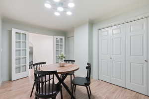 Dining area with light wood-style flooring, crown molding, arched walkways, and french doors