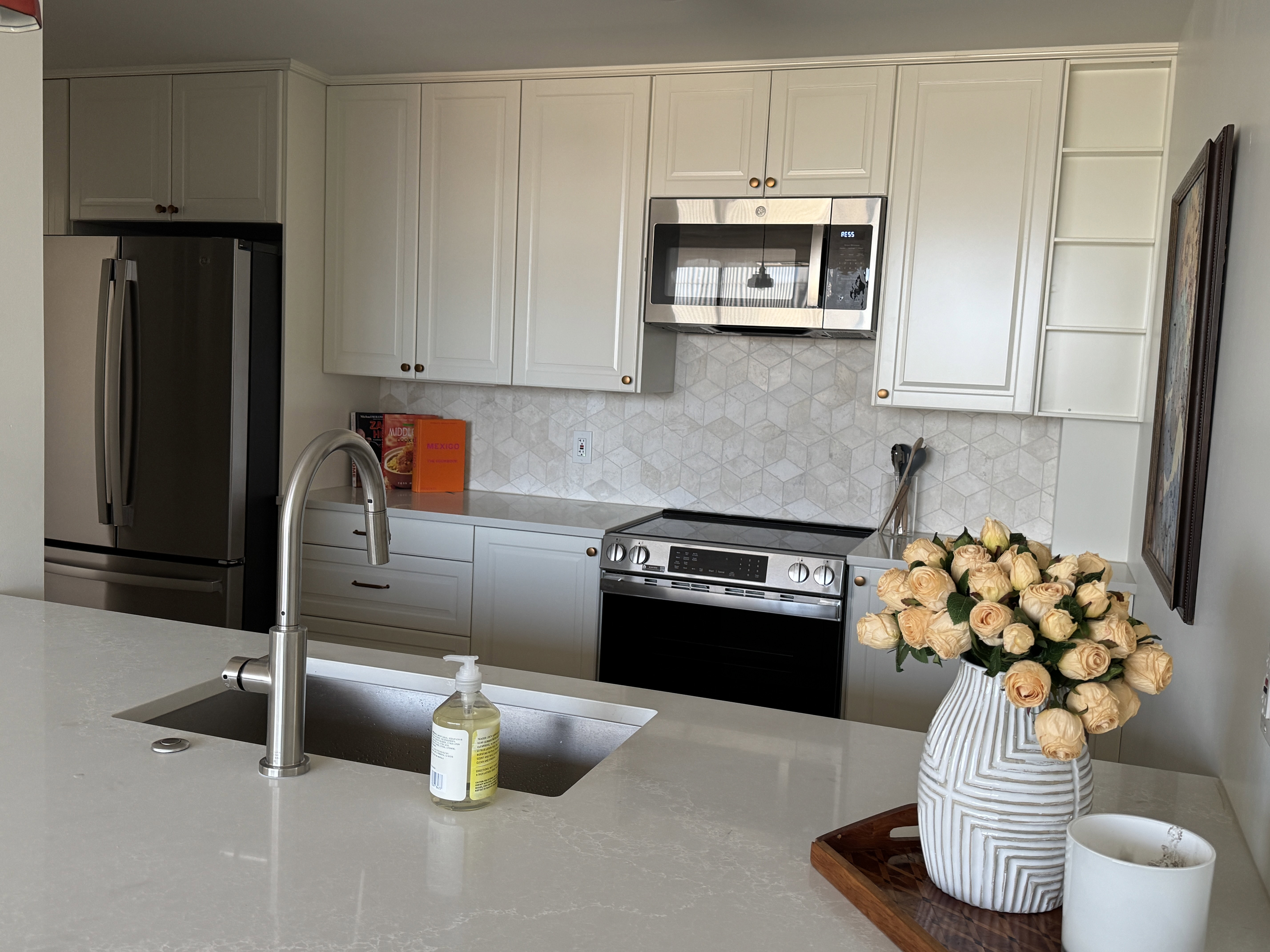 Contemporary kitchen featuring light shaker-style cabinetry, a geometric tile backsplash, and stainless steel appliances