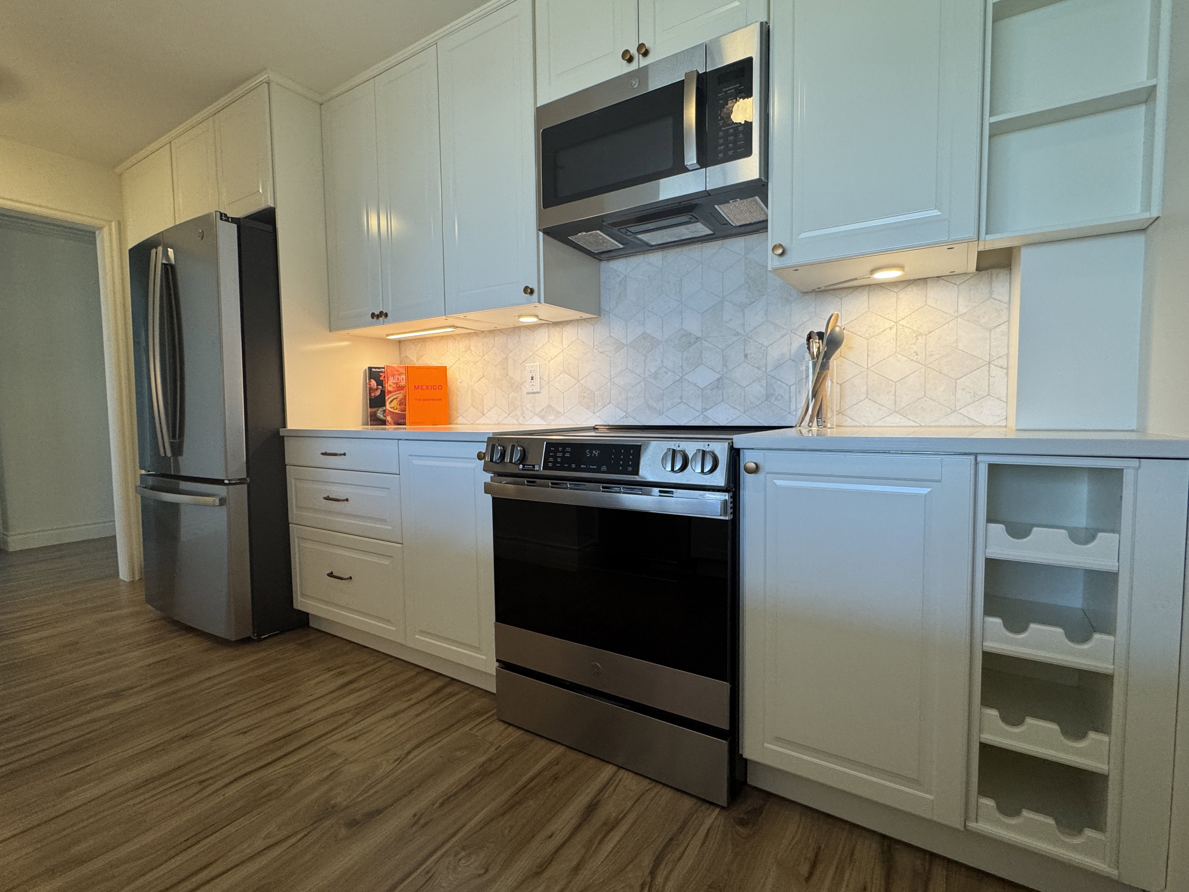 Kitchen featuring white cabinetry with full-height uppers, stainless steel appliances, geometric tile backsplash, and wood-finish flooring